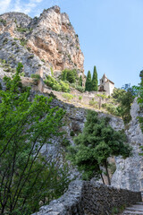 Fototapeta premium View on mountains cliff, old houses, green valley in remote medieval village Moustiers-Sainte-Marie in Provence, France