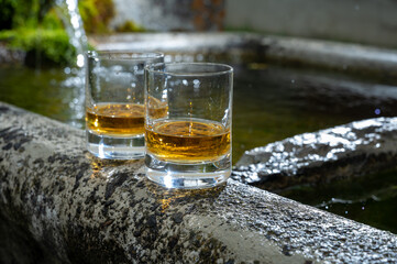Glasses of strong scotch single malt whisky served on old stone reservoir for water from mountain spring
