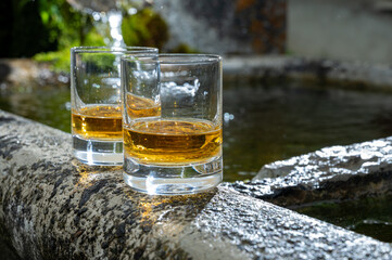 Glasses of strong scotch single malt whisky served on old stone reservoir for water from mountain spring