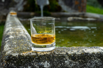 Glass of strong scotch single malt whisky served on old stone reservoir for water from mountain spring