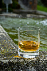 Glass of strong scotch single malt whisky served on old stone reservoir for water from mountain spring