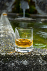 Glass of strong scotch single malt whisky served on old stone reservoir for water from mountain spring