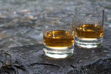Glass of strong scotch single malt whisky with fast flowing mountain river on background