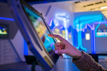 Woman hand using touchscreen display of floor standing tablet kiosk with city map in dark room of...