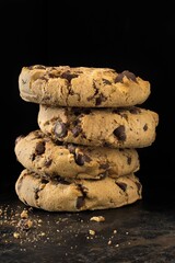 A stack of chocolate chip cookie biscuits and crumbs on a dark background