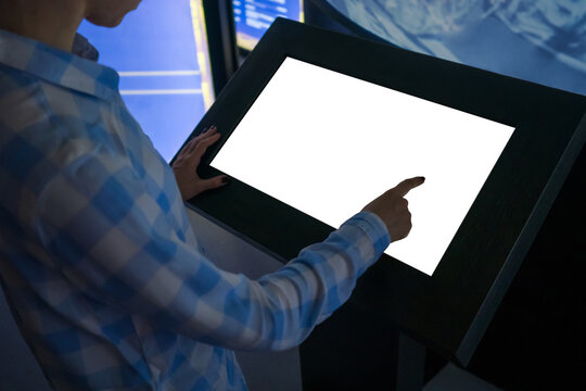 Mockup image - woman hand touching white empty interactive touchscreen display kiosk in dark room of modern technology museum. Mock up, template, scifi, education, futuristic and technology concept