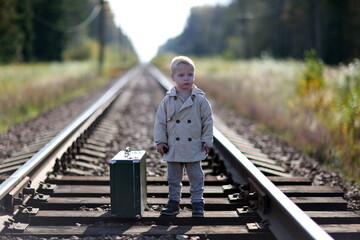 A child with a suitcase is standing on the railway. Travel