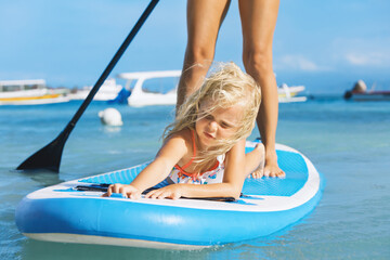 Active paddle boarder at sunset sea. Young mother with little clild paddling on stand up...