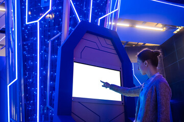 Woman hand using white blank interactive touchscreen display of electronic multimedia kiosk in dark room of scifi museum, exhibition: scroll, touch. Mock up, copyspace, template and technology concept