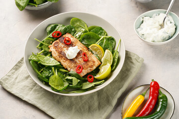A plate with fresh green raw spinach and fried wild salmon, lime slices, cream cheese sauce, red chilli pepper on grey concrete surface