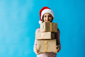 Happy little girl wearing christmas hat with a gift box isolated on blue background.