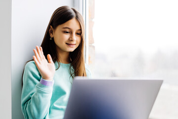 Teenage girl with laptop have video call sit on windowsill