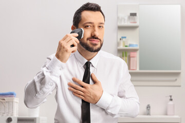 Man in a shirt and tie using a shaving machine in a bathroom