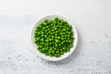 White plate with steamed green peas on a light blue background. Healthy delicious dietary...