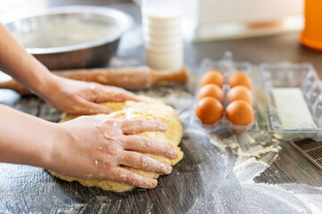 Female hands making dough for baking on wooden table near rolling pin, eggs and milk bottle. Culinary, cooking, baking concept