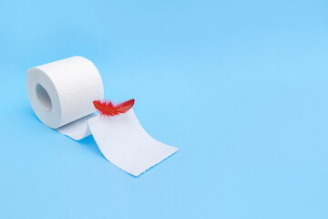 Red feather and toilet paper on light blue background. Hemorrhoid disease concept. Selective focus, copy space