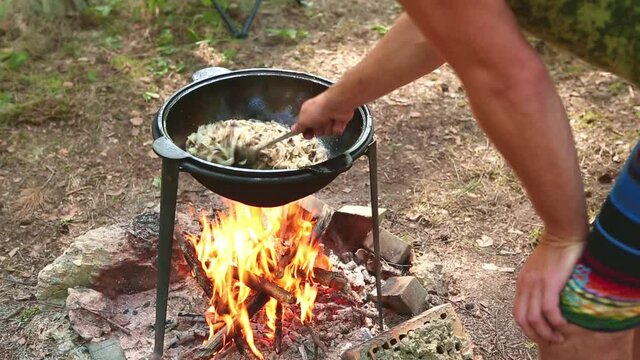 Cooking on a campfire in a cauldron outdoor in the woods camping on a hike. Stirring food in a camping kazan, smoke and aroma on an open fire. Outdoor recreation