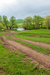 Rural dirt road in rural areas. Green fields, trees and a sky with beautiful clouds. Beautiful spring landscape.
