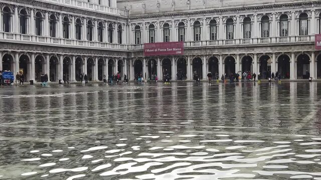 Venice, Italy - January 2022 - San Marco square submerged by high water on a sunny day while tourists are having fun with colored boots