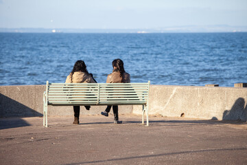 two young women sitting on a metal bench looking out to sea on Portobello beach in the pleasant...
