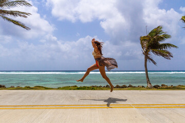 A happy woman jumps on the street in front of the ocean in san Andres Island, Colombia
