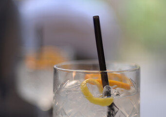 Selective focus on a crystal glass of gin and tonic with lemon, orange and black straw