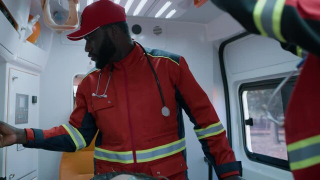 Multiracial man and woman in paramedic uniform preparing equipment while rescuing elderly patient in oxygen mask in emergency medicine vehicle