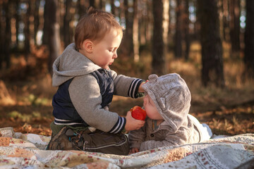 A two-year-old boy feeds his younger brother an apple.