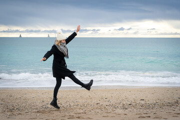 une femme sur une plage en hiver , donne un coup de pied en l'air - 478607043