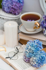 Fototapeta na wymiar A visual for content. Still life in vintage style. A mug with a drink, an old book, a cage, candles and hydrangea flowers in the garden on a white wooden table. The concept of a tea ceremony.