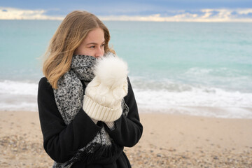 une jeune femme blonde qui a froid se met les mains dans son bonnet - 478607416