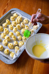 Smearing the dough with egg yolk and silicone brush. There is an egg yolk in the plate. Baking in the shape of a rose or snail. Home cooking. Close-up. Wooden table.