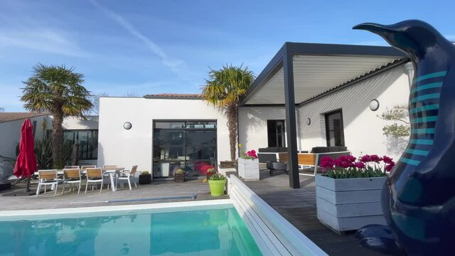 Trendy outdoor aluminium pergola, garden lounge, chairs, metal grill surrounded by landscaping and swimming-pool