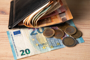 Black male wallet full of cash and twenty euro banknote with coins on a table