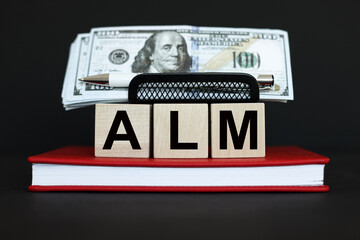 wooden blocks with dollar bills on a black background with text ALM conceptual symbol.