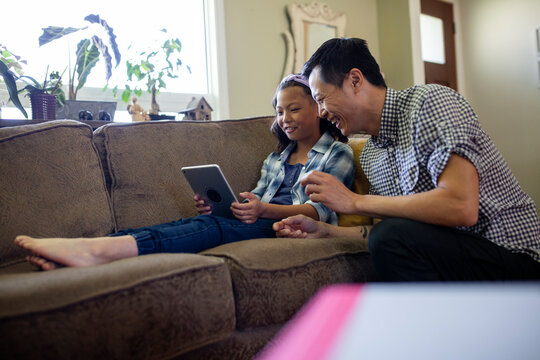 Father and daughter using digital tablet on living room sofa