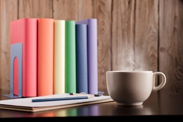 Cup of coffee or tea with hot steam in the morning, books with lgtbi flag colors, on the desk.