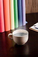 Cup of coffee or tea with hot steam in the morning, books with lgtbi flag colors, on the desk.