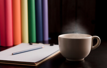 cup of coffee or tea with hot steam, books with lgtbi flag colors, on the desk.