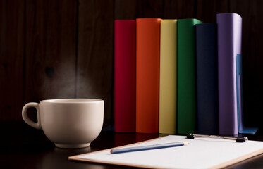 cup of coffee or tea with hot steam, books with lgtbi flag colors, on the desk.