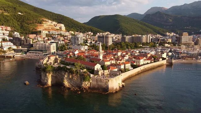 Historical part of the city washed by th sea from drone. Buildings with red roofs. Mountains in the background. Drone Shot of old town Budva in Montenegro.