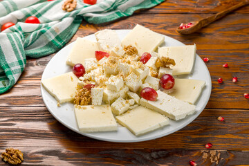 Suluguni cheese sliced on a plate with grapes and walnuts on wooden table