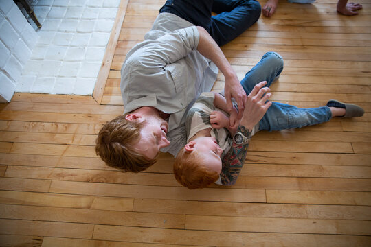 Playful father tickling son on hardwood floor