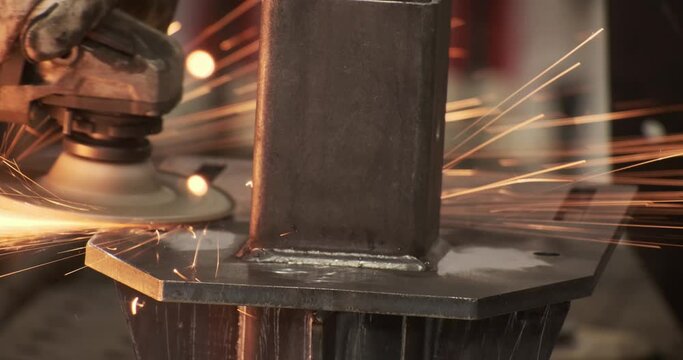 Closeup craftsman hands welding seams with angle grinder working at manufacture fabric. Welder in protective gloves make metallic production surrounded by spark illumination. Metallurgical workshop