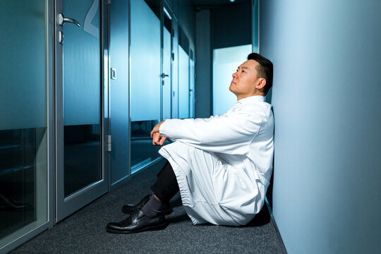 Upset and thinking asian man sitting on the floor in the laboratory, frustrated scientist