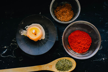 spices and herbs on spoons burning candle on black background