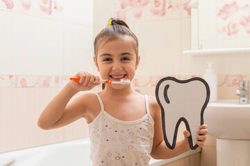 The girl is brushing her teeth, holding a cardboard tooth in her hands. Oral hygiene.