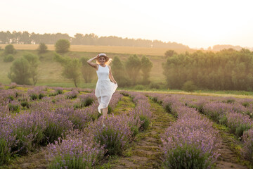 Beautiful young healthy woman with a white dress running joyfully through a lavender field, straw hat