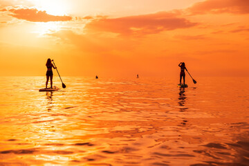 Travelers on stand up paddle board at quiet sea with sunset or sunrise. Girls on Red Paddle sup...