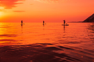 Travelers on stand up paddle board at quiet sea with sunset or sunrise. Girls on Red Paddle sup board and sunset